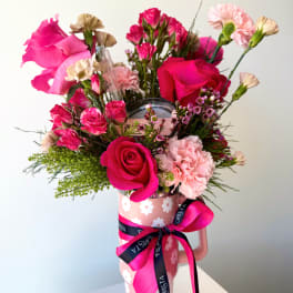 Pink roses and carnations arranged in a decorated vase with a ribbon