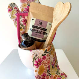 Gift basket with pancake mix, syrup, wooden spoon, and floral oven mitts