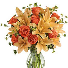 Orange roses and pale lilies in a clear glass vase