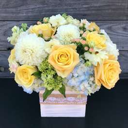 Yellow roses and white blooms arranged in a white box
