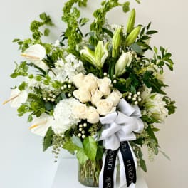 White roses and lilies arranged in a glass vase with a white ribbon