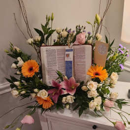 Floral sympathy arrangement around an open book with orange gerberas and pink lilies