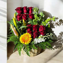 Basket arrangement of red roses, yellow lily buds, and a yellow gerbera daisy