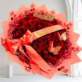 Large bouquet of red roses wrapped in pink paper with a ribbon and crown