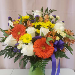 Mixed bouquet of white roses, orange gerberas, and yellow daisies in a green vase
