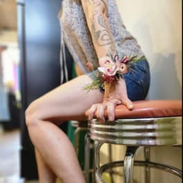 Woman wearing a floral wrist corsage and orange clogs seated on a stool