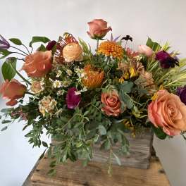 Mixed bouquet of peach roses, orange blooms, and small white daisies in a wooden box