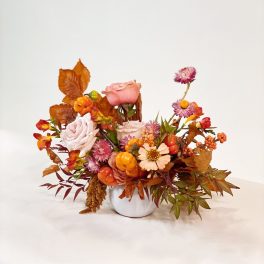 Autumn floral arrangement in a white vase with pink roses and orange accents