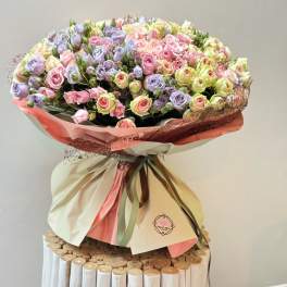 Large bouquet of pastel pink and lavender roses wrapped in cream and pink paper