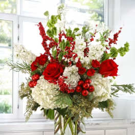 Red roses and white hydrangeas in a clear glass vase with red berry accents