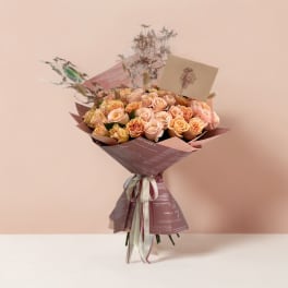Bouquet of peach and blush roses wrapped in mauve paper