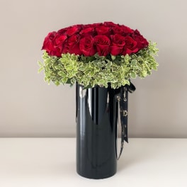 Red roses arranged in a black vase with variegated greenery