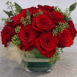 Red roses arranged in a square glass vase with a sheer ribbon bow
