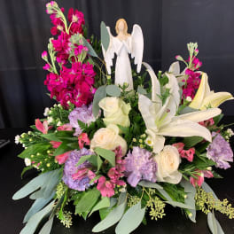 Large floral arrangement with white lilies, roses, and pink blooms around an angel figurine