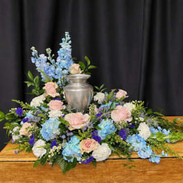 Pastel floral arrangement with roses, hydrangeas, and carnations around a silver urn