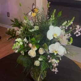 Large mixed floral arrangement in a glass vase with white orchids and roses