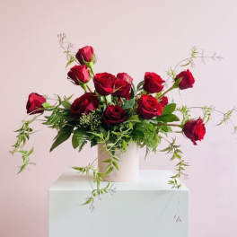 Red roses arranged in a white vase with trailing greenery