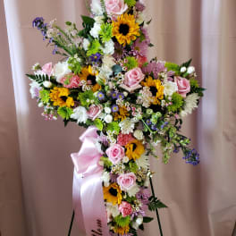 Large floral cross with pink roses, sunflowers, and white daisies on a stand