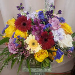 Mixed bouquet of roses, gerbera daisies, and purple filler flowers in a vase