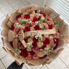 Large bouquet of red, pink, and cream roses wrapped in beige paper