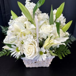 White floral arrangement in a woven basket with lilies and roses