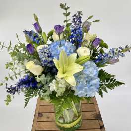 Blue and purple floral arrangement with lilies and hydrangeas in a glass vase