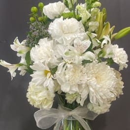 White flowers arranged in a clear glass vase with a sheer ribbon.