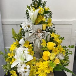 Tiered yellow and white floral arrangement with an angel figurine centerpiece