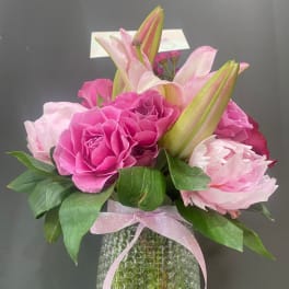Pink roses and lilies arranged in a textured glass vase with a ribbon.