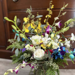 Mixed bouquet with white roses, orchids, and yellow accents in a glass vase