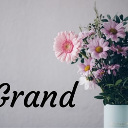 Pink and lavender daisies in a light blue vase with the word Grand