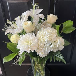 White lilies, roses, and hydrangeas in a glass vase