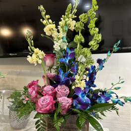 Pink roses and blue orchids in a wooden box with greenery