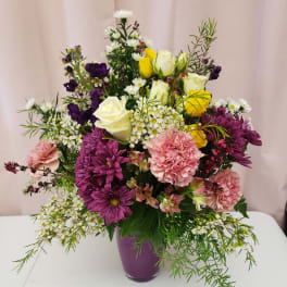 Mixed bouquet in a purple vase with roses, carnations, and purple daisies