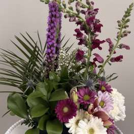Mixed floral arrangement with purple and white blooms in a black container