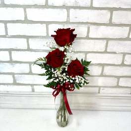 Three red roses in a clear glass vase with baby's breath and a red ribbon