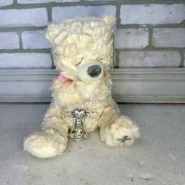 Cream teddy bear with a pink ribbon and decorative charm