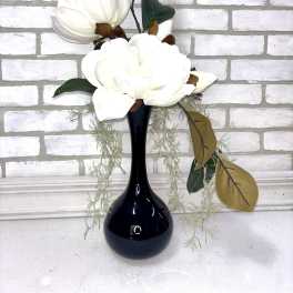 White magnolia stems in a black vase with trailing greenery
