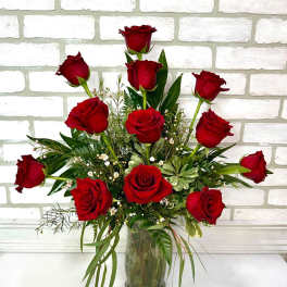 Red roses arranged in a clear glass vase with greenery