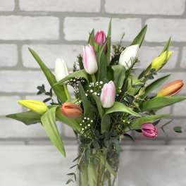 Tall clear vase of mixed pink, white, yellow, and orange tulips with filler flowers