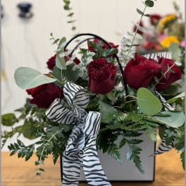 Red roses in a white box with zebra-print ribbon and greenery