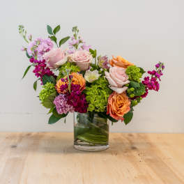 Mixed bouquet of pink, orange, and green flowers in a glass vase