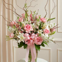 Tall arrangement of pink roses and white lilies in a glass vase with a large pink ribbon bow