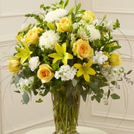 Tall yellow and white flower arrangement with roses and lilies in a clear glass vase