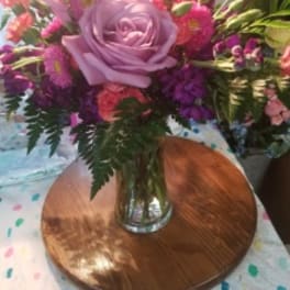 Pink and purple flower arrangement in a clear glass vase on a wooden stand