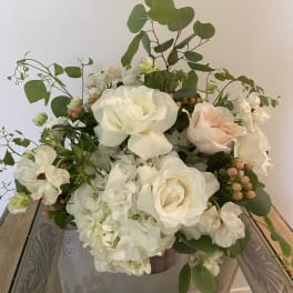 White roses and hydrangeas arranged in a vase with greenery and peach berries.