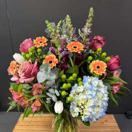 Mixed bouquet in a glass vase with pink roses, orange gerberas, and blue hydrangea