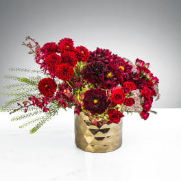 Low arrangement of deep red and burgundy flowers in a faceted gold vase