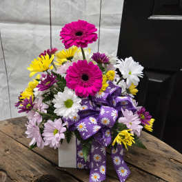 Colorful daisy bouquet in a white box with a purple ribbon