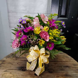 Mixed bouquet of pink, purple, and yellow flowers with a large yellow ribbon